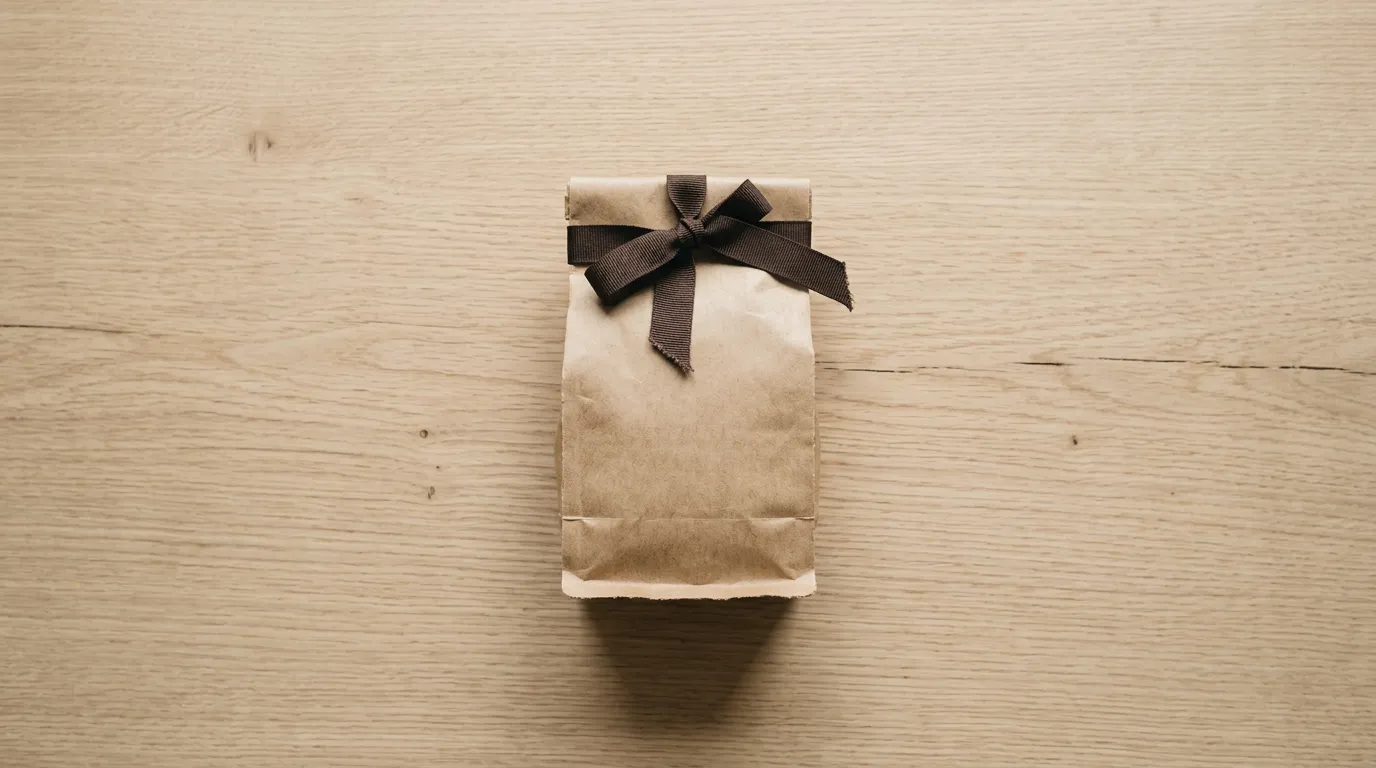 A kraft paper coffee bag tied with a dark ribbon bow on a light wood surface